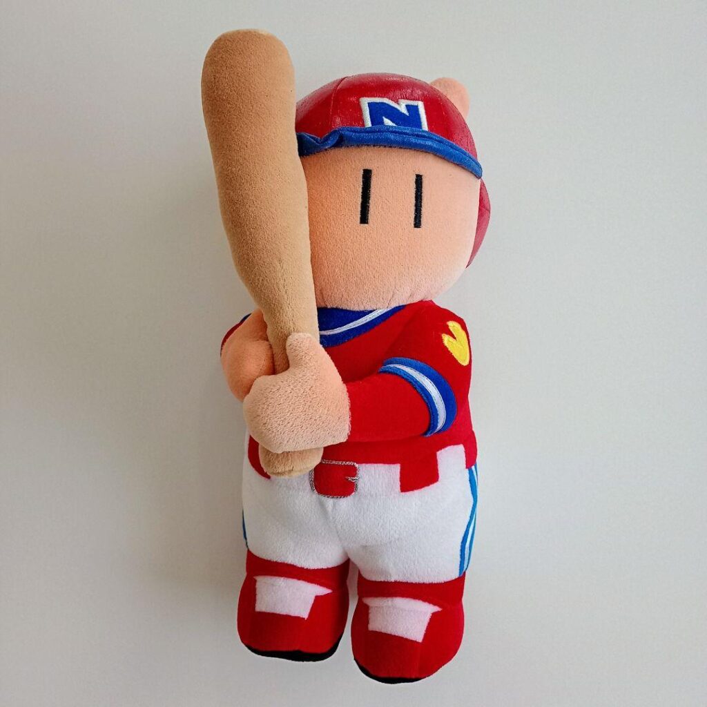 A plush toy of Famista-kun, a baseball player mascot for Namco's Family Stadium series of video games. He has a red hat and uniform and is holding a bat. An N is on his hat and a Pac-Man logo is on his shoulder.